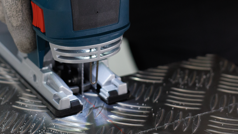 PRO Alu T127D 직쏘날, 100mm, 5개 안전 장비를 착용한 사람이 퍼즐을 조작하여 무늬가 있는 금속판을 자르고 있습니다.