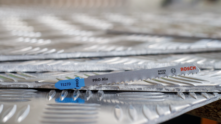 PRO Alu T127D 직쏘날, 100mm, 5개 질감이 있는 금속판을 쌓아 놓은 위에 톱날을 올려놓은 모습입니다.