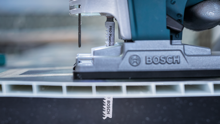 근접 촬영된 작업장 장면에서 퍼즐이 두꺼운 플라스틱 패널을 자르고 있습니다.