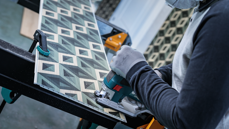 안전 장비를 착용한 사람이 휴대용 톱으로 무늬가 있는 보드를 자릅니다.