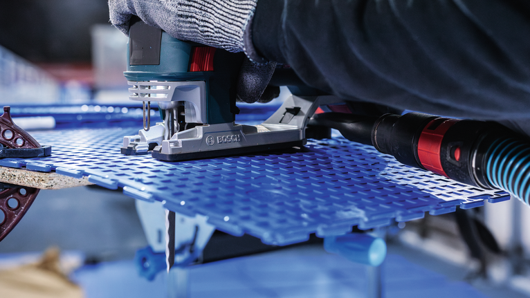 안전 장비를 착용한 사람이 퍼즐을 조정하여 파란색 천공 시트를 자르고 있습니다.