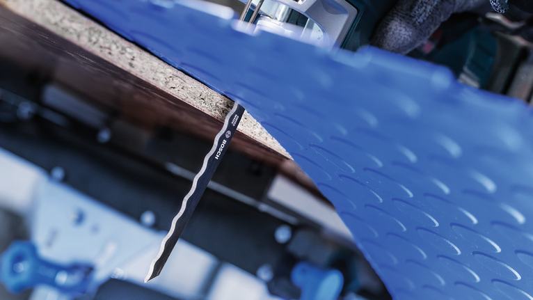 안전 장비를 착용한 사람이 퍼즐을 사용해 파란색 플라스틱 시트를 자르고 있습니다.