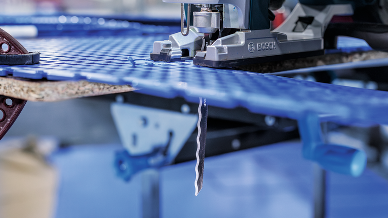 작업장에서 파란색 플라스틱 시트를 퍼즐로 자르고 있는 모습입니다.