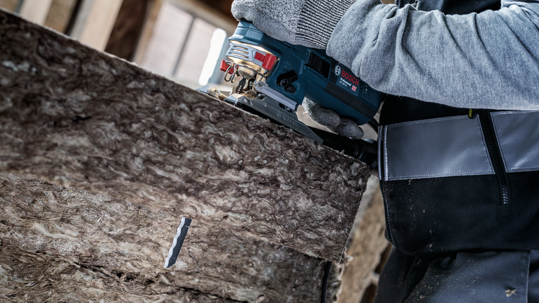 안전 장비를 착용한 사람이 톱으로 단열재를 자르고 있습니다.