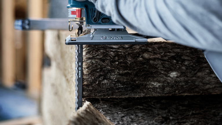 안전 장비를 착용한 사람이 톱을 사용하여 두꺼운 단열재를 자릅니다.