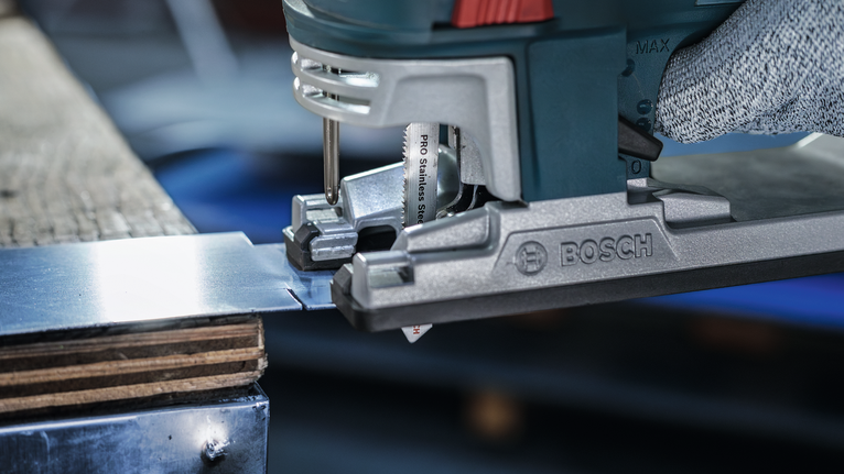 안전 장비를 착용한 사람이 퍼즐 톱으로 금속판을 자릅니다.