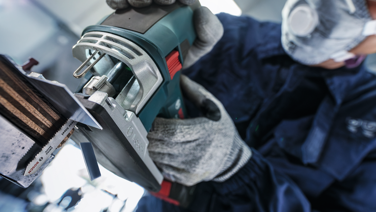 안전 장비를 착용한 사람이 전동 공구를 조작하여 금속 조각을 자르고 있습니다.