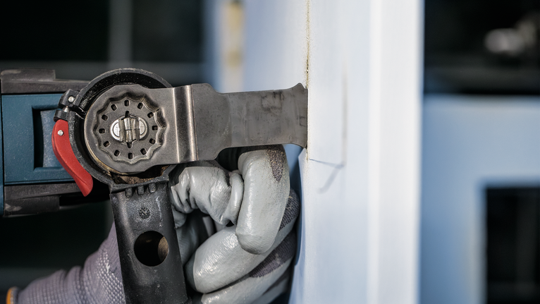 안전 장비를 착용한 사람이 전동 공구를 사용해 벽을 자르고 있습니다.