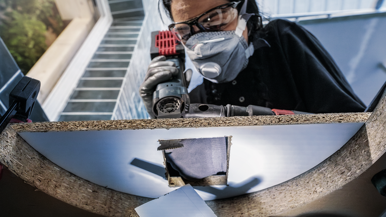 안전장비를 착용한 사람이 나무판에 구멍을 뚫고 있습니다.