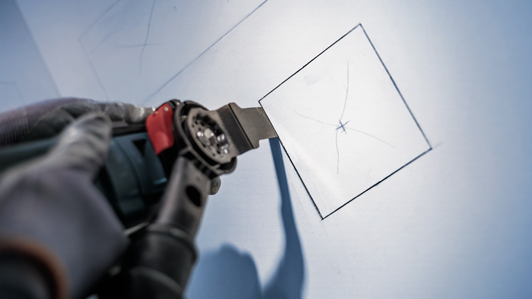 안전 장비를 착용한 사람이 전동 공구를 사용해 건식벽체를 정사각형으로 자릅니다.