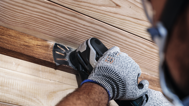 안전 장비를 착용한 사람이 전동 공구로 나무판을 연마하고 있습니다.