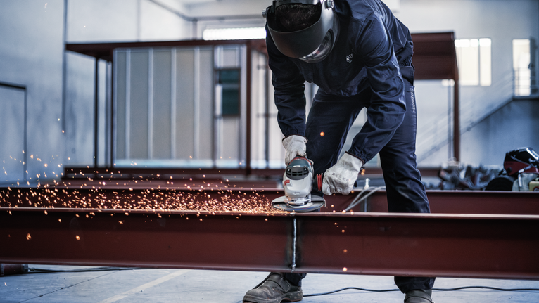 안전 장비를 착용한 사람이 금속 막대를 갈아서 불꽃을 낸다.