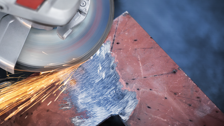 금속판 가장자리를 연마하는 동안 불꽃을 생성하는 각도 그라인더입니다.