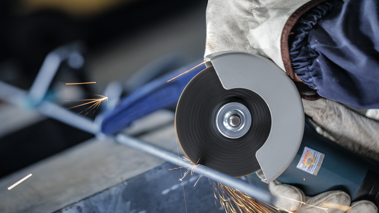 안전 장비를 착용한 사람이 절단 도구로 금속 막대를 갈고 있습니다.