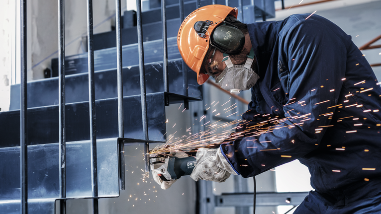 안전장비를 착용한 사람이 금속 계단을 갈아서 불꽃을 바깥쪽으로 뿜어낸다.