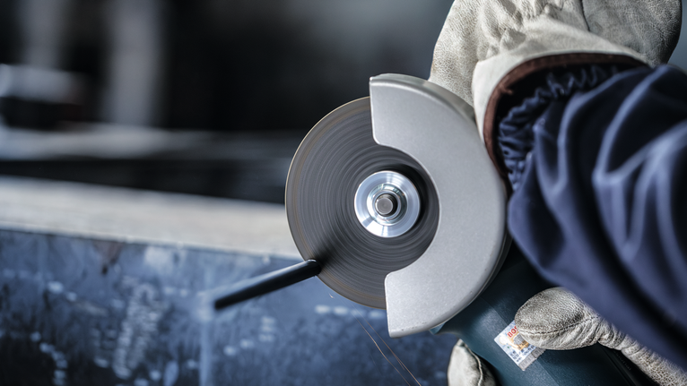 안전 장비를 착용한 사람이 각도 분쇄기를 사용하여 금속을 절단합니다.