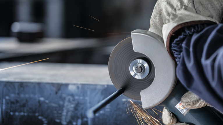 안전 장비를 착용한 사람이 각도 분쇄기로 금속을 자르면서 불꽃을 일으킵니다.