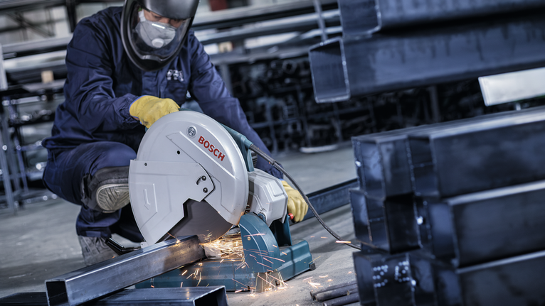 안전 장비를 착용한 작업자가 전기톱으로 금속 파이프를 자르면서 불꽃이 튀었습니다.