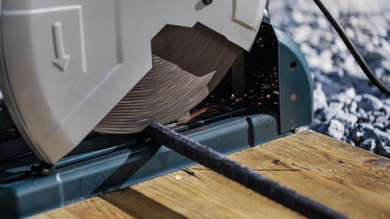 나무 플랫폼 위에 있는 금속 막대를 자르는 절단 톱입니다.