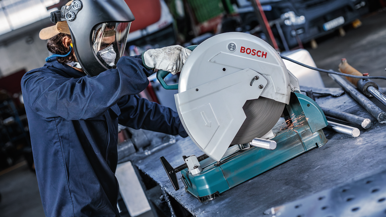 안전 장비를 착용한 사람이 고정된 원형 톱으로 금속 파이프를 자릅니다.