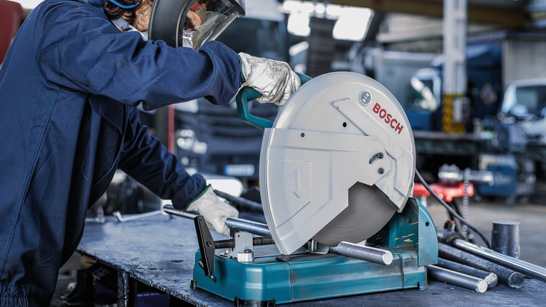 안전 장비를 착용한 사람이 원형 톱을 조작하여 금속 파이프를 절단하고 있습니다.