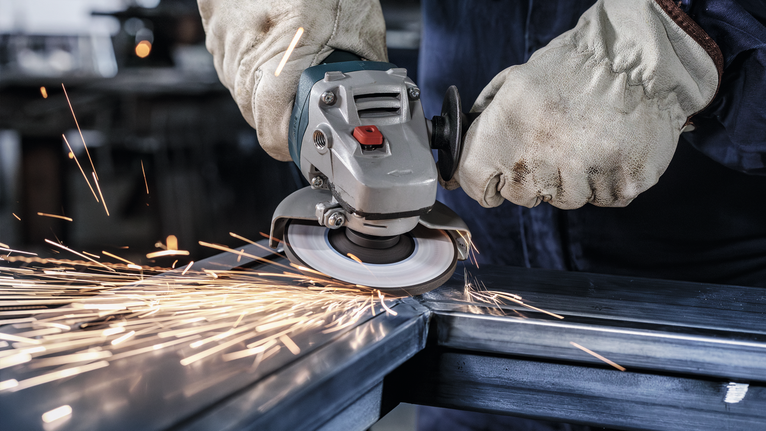 안전 장비를 착용한 사람이 각도 분쇄기를 사용하여 금속을 절단하면서 불꽃이 발생합니다.