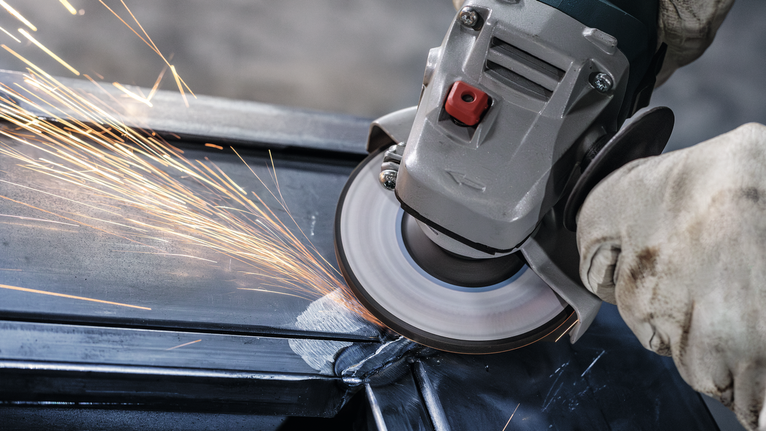 안전 장비를 착용한 사람이 금속을 갈아서 밝은 불꽃을 낸다.