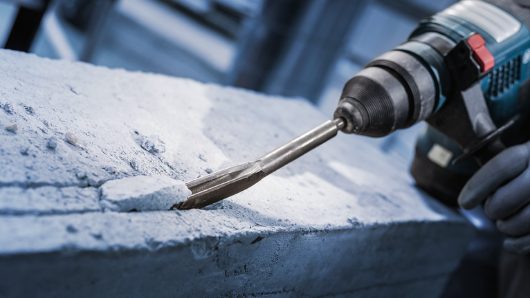 안전 장비를 착용한 사람이 회전 망치로 콘크리트를 깎고 있습니다.