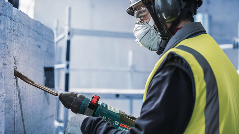 안전 장비를 착용한 사람이 전동 공구로 콘크리트를 깎고 있습니다.