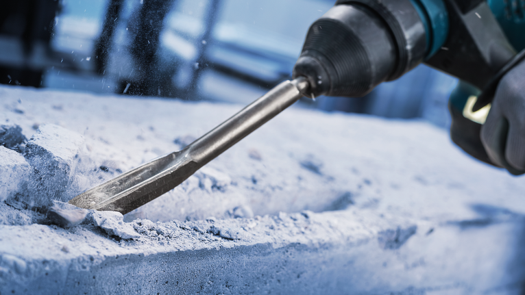 안전 장비를 착용한 사람이 회전 망치를 사용하여 콘크리트를 깎고 있습니다.