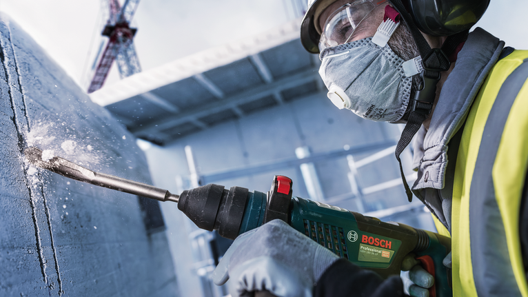 안전 장비를 착용한 사람이 건설 현장에서 콘크리트에 구멍을 뚫고 있습니다.