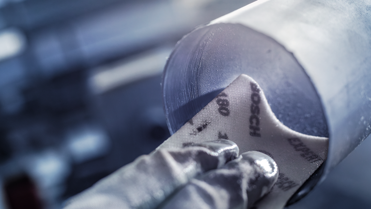 EXPERT W480 Web 1/4 핸드 샌딩 시트, 115 x 140mm, G120 안전장비를 착용한 사람이 금속 파이프의 내부를 샌딩하고 있습니다.