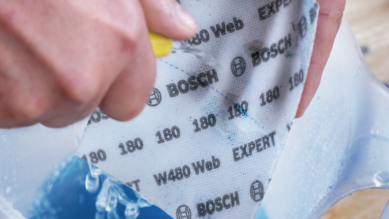 EXPERT W480 Web 1/4 핸드 샌딩 시트, 115 x 140mm, G120 안전 장비를 착용한 사람이 용기에 사포를 적셔 문지르고 있습니다.