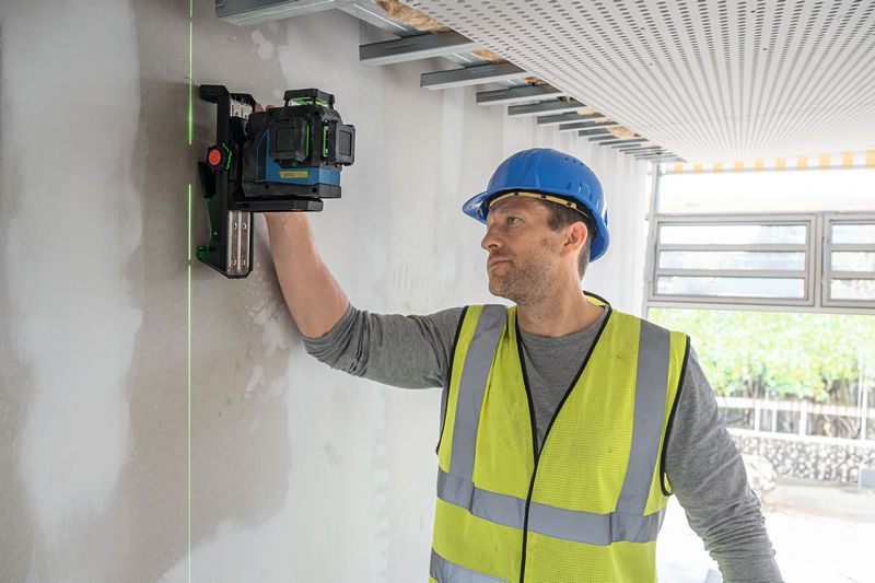 안전 장비를 착용한 사람이 레이저 레벨링 도구를 벽에 정렬하고 있습니다.