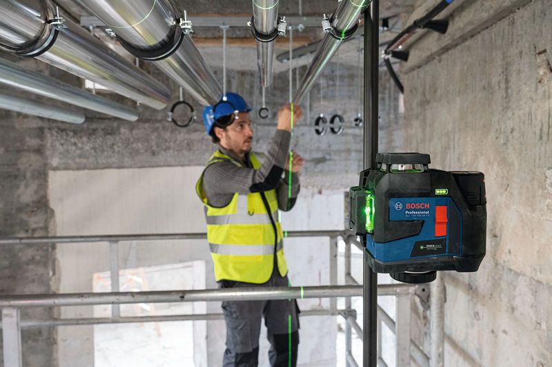 안전장비를 착용한 사람이 레이저 레벨링 도구를 사용하여 파이프를 정렬하고 있습니다.