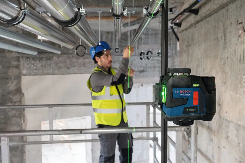 안전장비를 착용한 사람이 레이저 레벨링 도구를 사용하여 파이프를 정렬하고 있습니다.