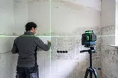 한 사람이 삼각대에 녹색 레이저 레벨링 도구를 올려놓고 벽에 타일을 정렬하고 있습니다.