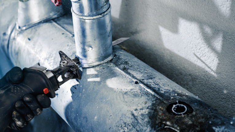 안전 장비를 착용한 사람이 왕복톱으로 금속 파이프를 자릅니다.