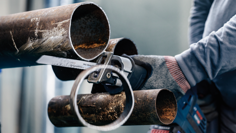 안전 장비를 착용한 사람이 왕복톱으로 금속 파이프를 자릅니다.