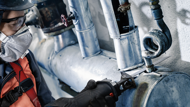 안전 장비를 착용한 사람이 왕복톱으로 금속 파이프를 자릅니다.