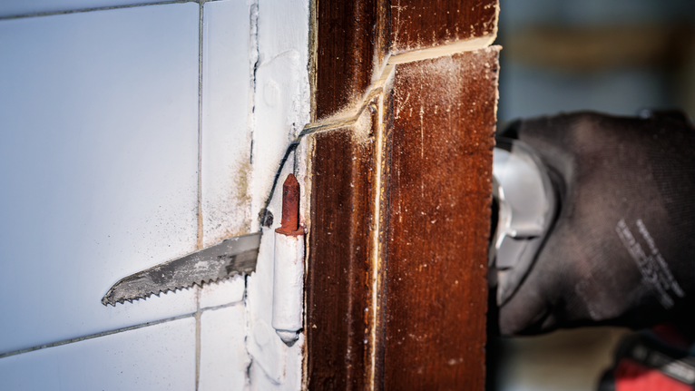 안전 장비를 착용한 사람이 전동 공구를 사용하여 나무 문틀을 자르고 있습니다.