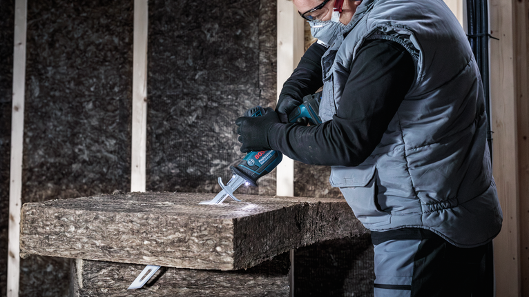 안전 장비를 착용한 사람이 전기톱으로 단열재를 자르고 있습니다.