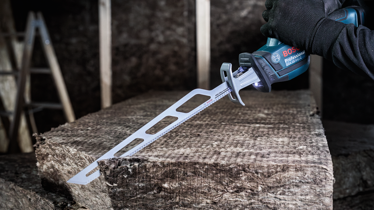 안전 장비를 착용한 사람이 왕복톱을 사용하여 단열재를 절단하고 있습니다.