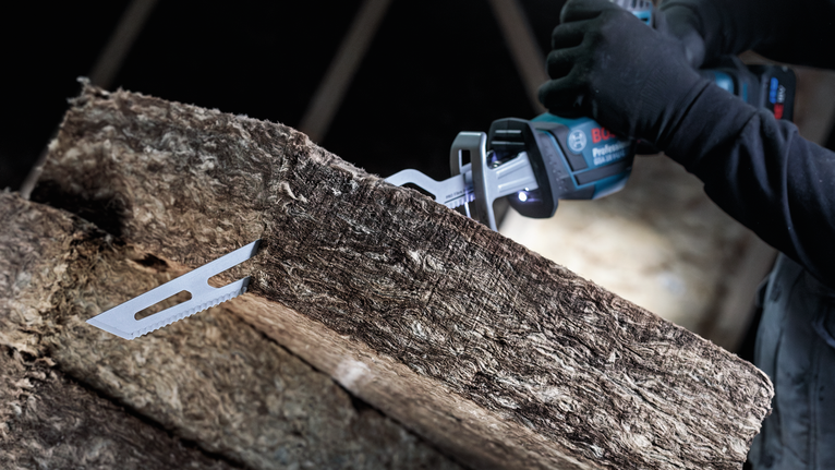 안전 장비를 착용한 사람이 왕복톱을 이용해 단열재를 절단하고 있습니다.