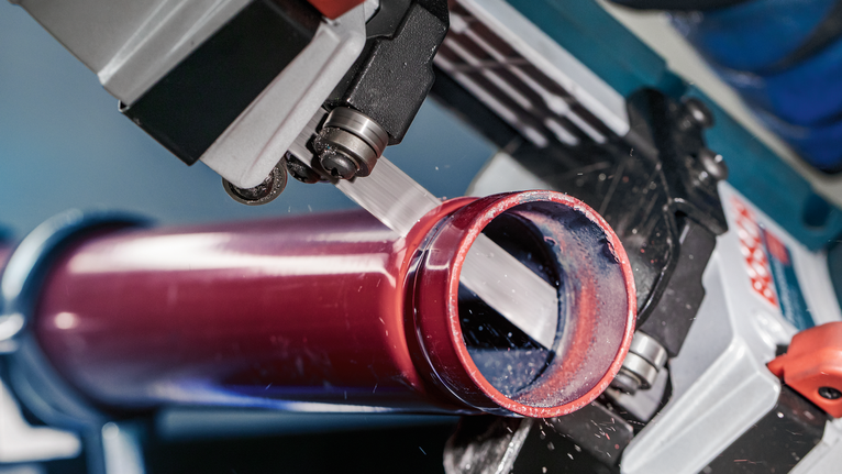 PRO CB2824 Band 톱날, 733mm, 2개 작업장에서 밴드톱이 붉은 금속 파이프를 자르고 있습니다.