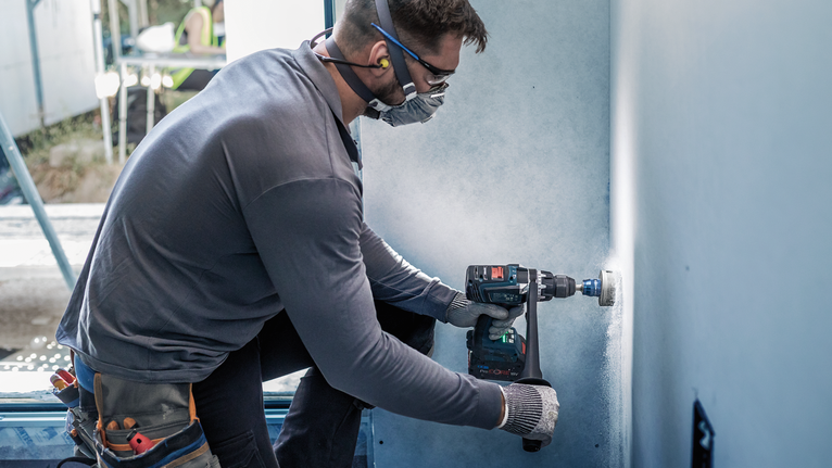 안전장비를 착용한 사람이 벽에 원형 구멍을 뚫습니다.