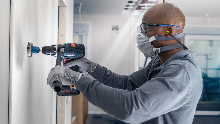 안전 장비를 착용한 사람이 전동 드릴을 사용하여 벽을 자르고 있습니다.