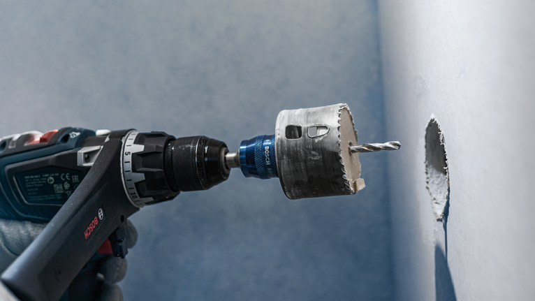 안전 장비를 착용한 사람이 홀 톱으로 벽에 원형 구멍을 뚫고 있습니다.