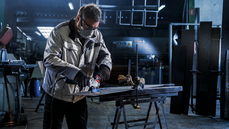 PRO Metal clean X-Lock 컵 브러시, 75 x 0.3mm 안전 장비를 착용한 사람이 작업장의 작업대에서 금속을 갈고 있습니다.