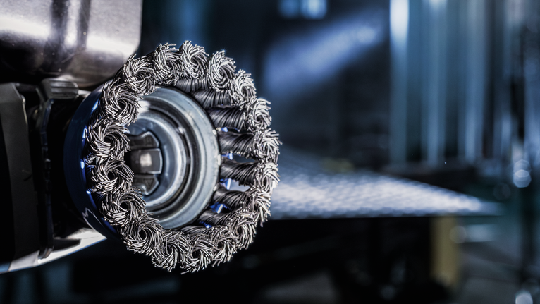 작업장의 전동 공구에 장착된 와이어 브러시 휠 부착물의 클로즈업.